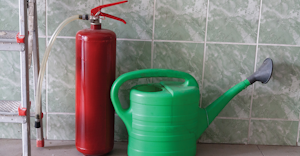 “Watering can and fire extinguisher stand in front of wall”