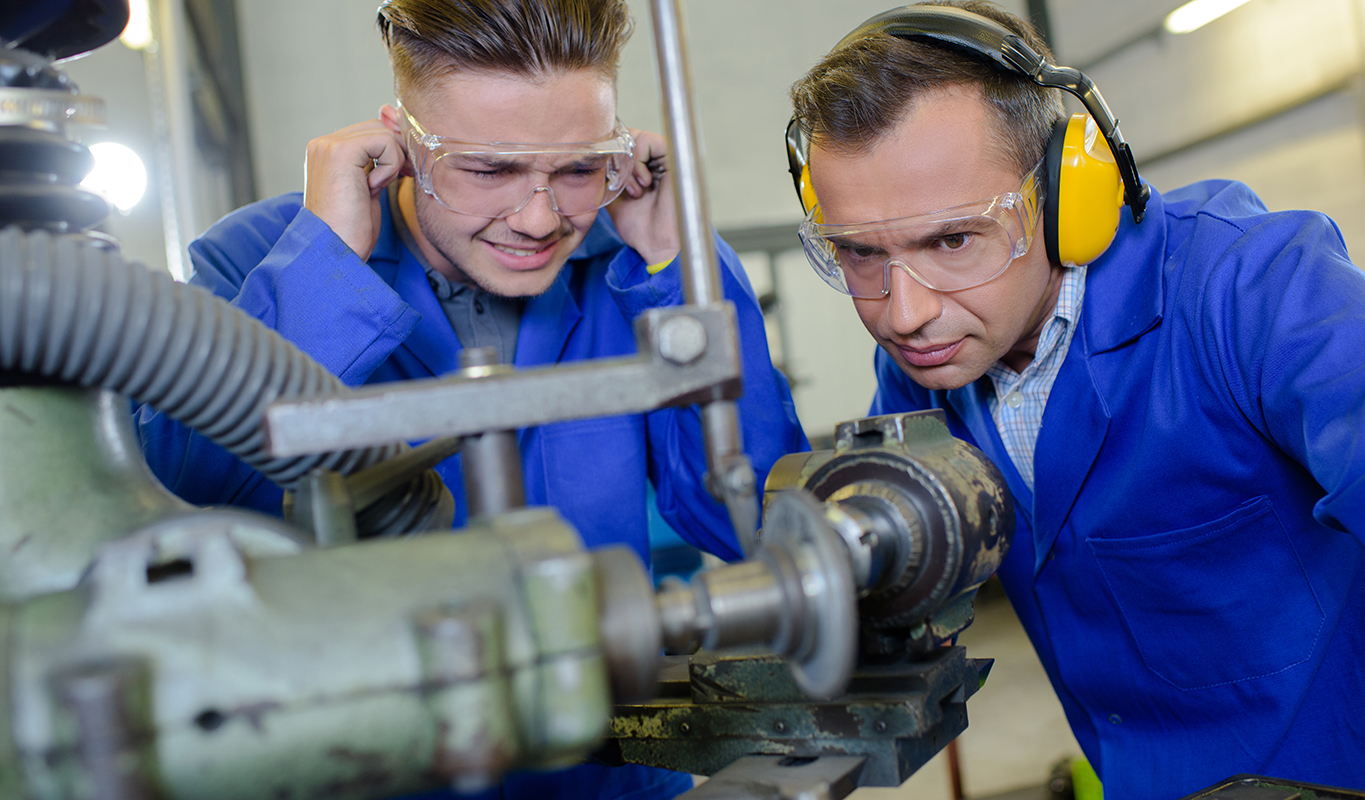 Apprentice with instructor protecting ears from noisy CNS machine.