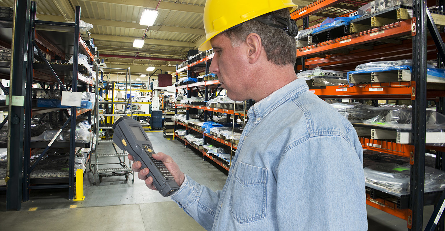 A worker is using a handheld scanner for inventory management control in a manufacturing warehouse operation.