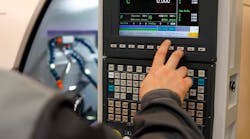 CNC machine operator entering a program at a control panel. CNC machine operator entering a program at a control panel.
