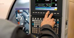 CNC machine operator entering a program at a control panel. CNC machine operator entering a program at a control panel.