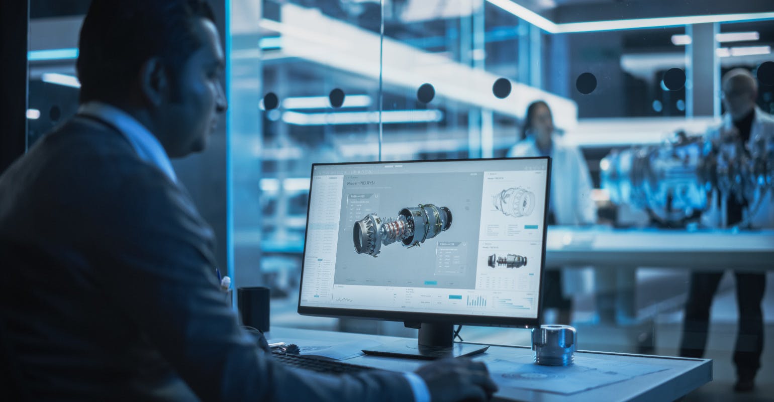 Designer working on CAD program for turbine engine, at desktop computer in plant.