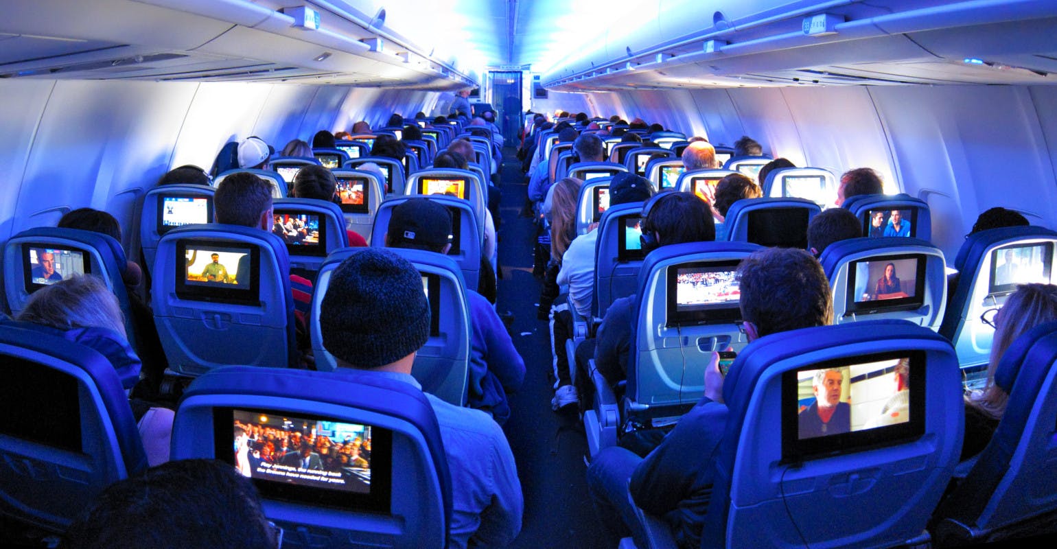 Airline passengers flying coach on a commercial flight with built in screens.