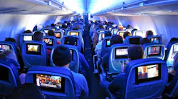 Airline passengers flying coach on a commercial flight with built in screens.