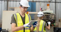 Engineer uses tablet while behind co-worker operates CNC machine. Engineer uses tablet while behind co-worker operates CNC machine.