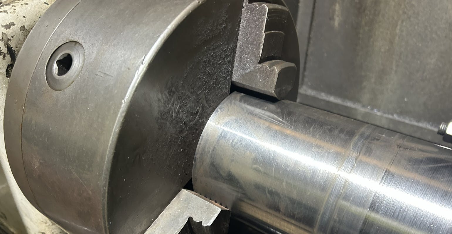 Lathe chuck holding steel bar for turning.