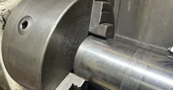 Lathe chuck holding steel bar for turning.
